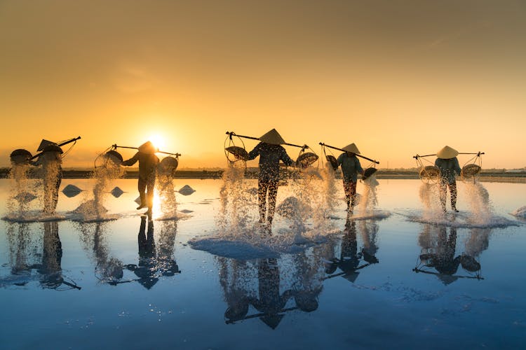 People Pouring Sea Water On Salt Field During Sunset