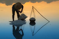 一张宁静的照片捕捉到了日出时分盐农劳作的景象，水面上映出美丽的倒影