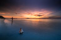 在日落时分的海滩上，宁静而孤独的身影映衬着沙滩和贝壳，营造出一种平和、反射的景象