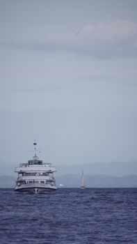 A cruise ship and sailboat navigate the serene waters of Bodensee lake on a tranquil day.