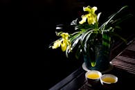 黑暗背景中，两个茶杯旁的花瓶里，黄色兰花静静绽放