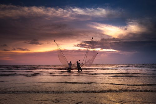 Двое мужчин стоят на водоеме и держат рыболовные сети