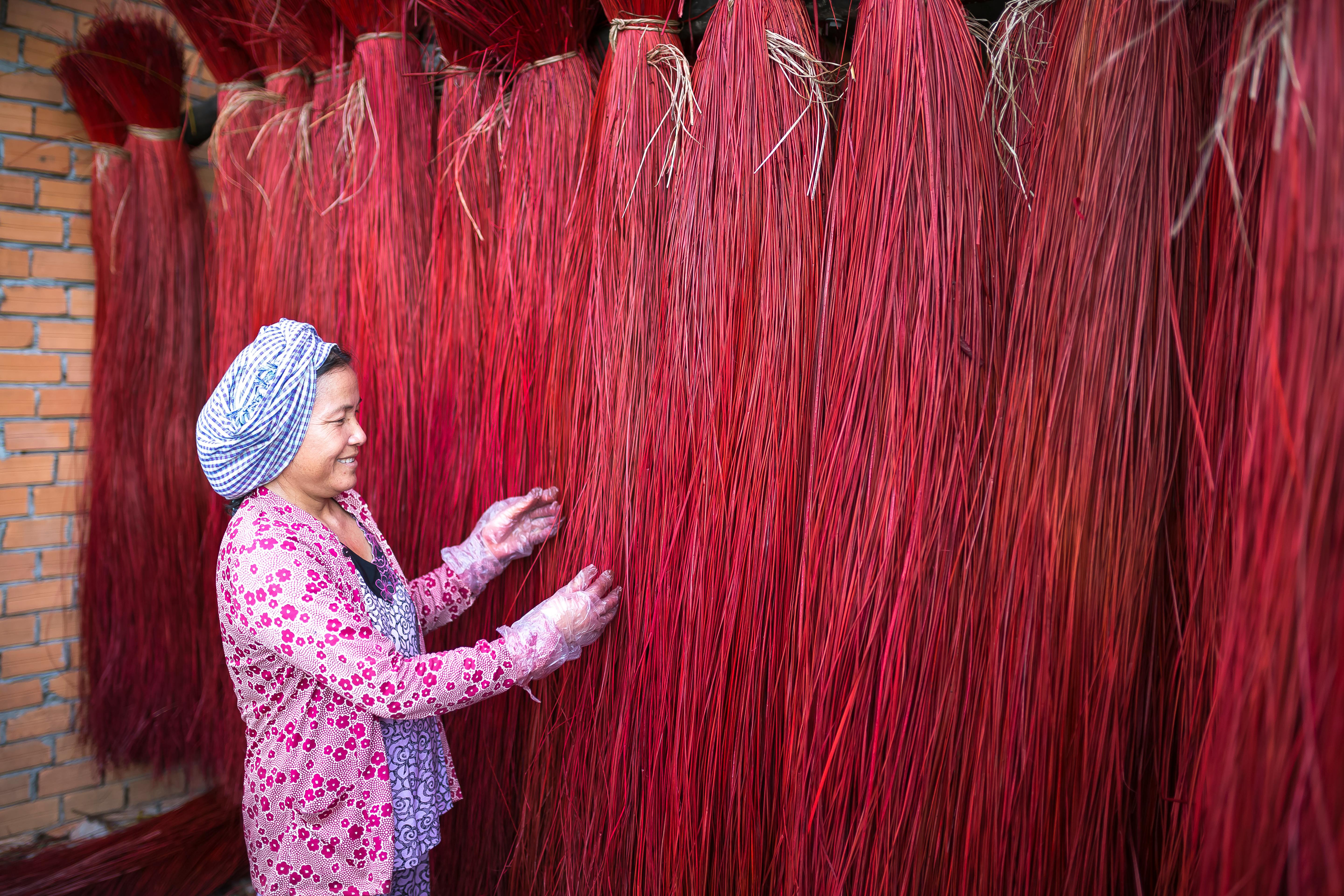 一位身着传统服装的女子正在室内检查悬挂的红色扫帚纤维