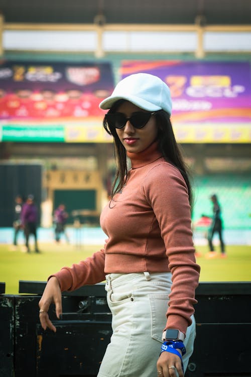 A woman in a white hat and sunglasses standing in front of a stadium