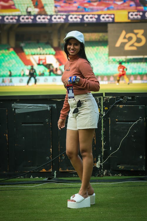 A woman in shorts and a hat standing on the field