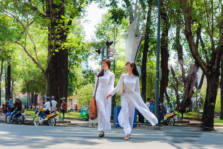 Photo Of Two Women In White Outfits Holding Hands While Crossing The Street