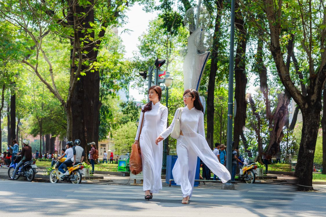 Photo of Two Women In White Outfits Holding Hands While Crossing the ...