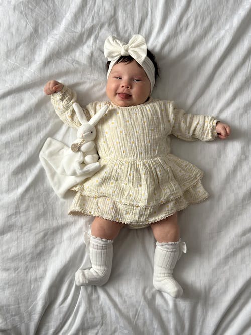 Free A baby girl laying on a bed wearing a white dress Stock Photo