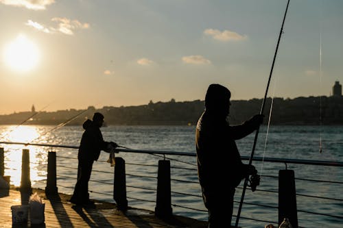 Two people fishing at sunset on a pier
