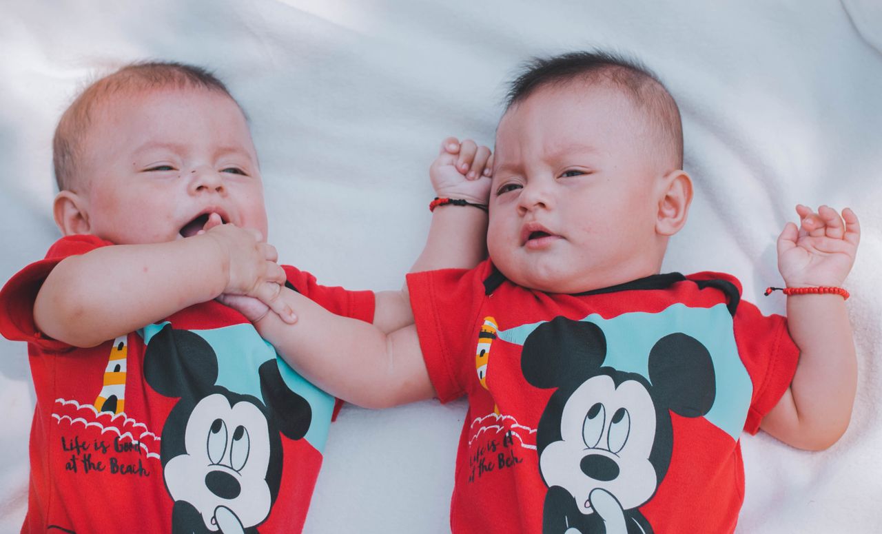 cute twin babies wearing matching red t shirts enjoying a moment indoo