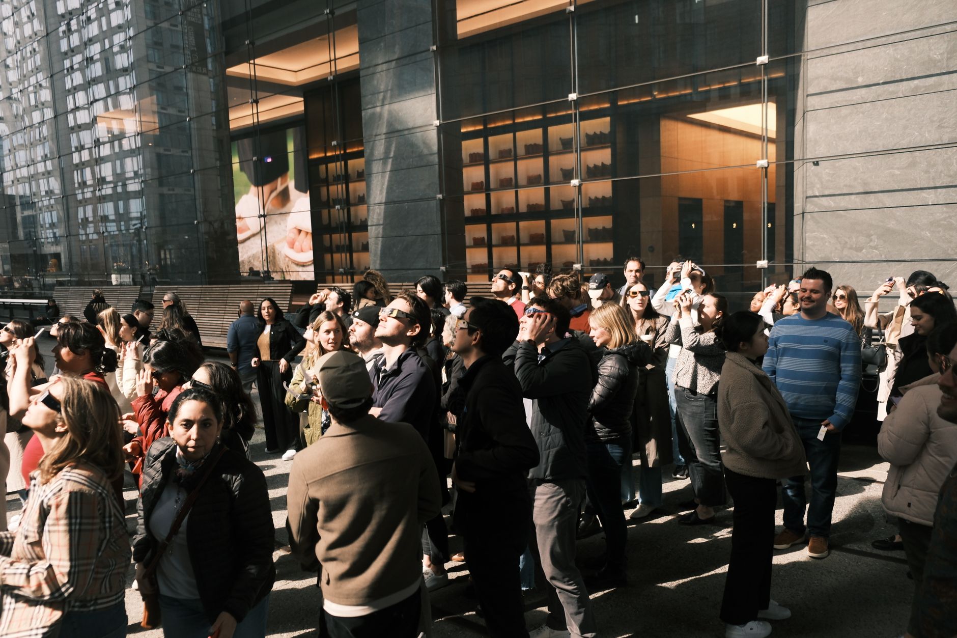 People gathered outside a glass-walled modern building during the day, observing an event.