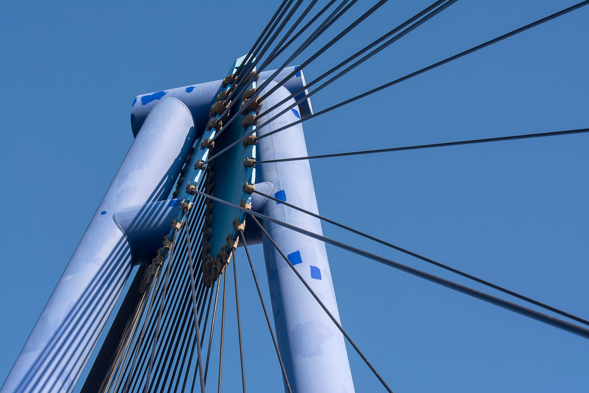 Close-up of a modern suspension bridge's cables and tower against a clear blue sky.