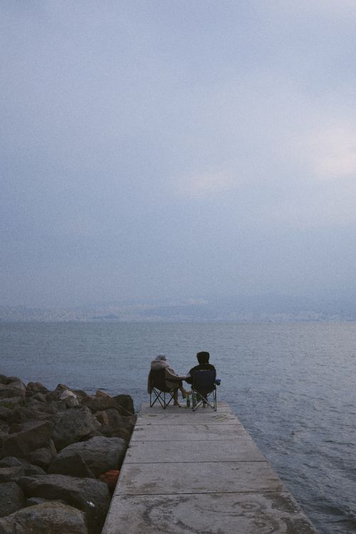Free Two people enjoying a serene moment by the sea on a pier in İzmir, Türkiye. Stock Photo