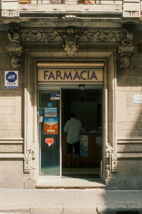 Free Architectural details of a historic pharmacy entrance in Madrid, Spain, featuring a lone customer inside. Stock Photo