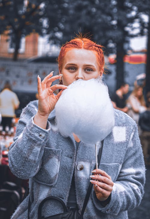 Free A Woman Eating Cotton Candy at a Festival in a City  Stock Photo