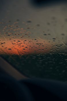 Raindrops on a car window with a vibrant sunset in the background, creating a serene ambiance.