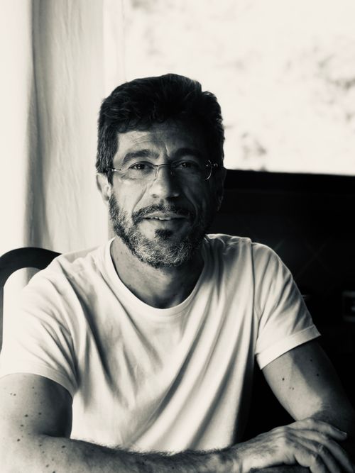 Free Close-up portrait of a bearded man wearing glasses and a white shirt, smiling indoors. Stock Photo
