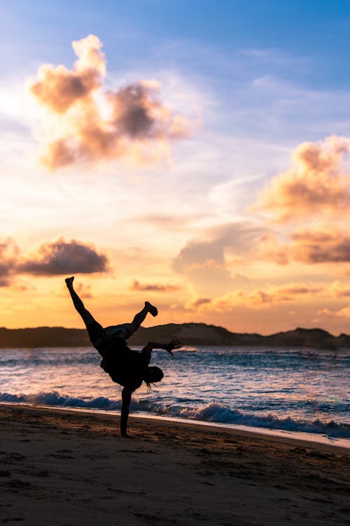 A man doing a handstand on the beach at sunset
