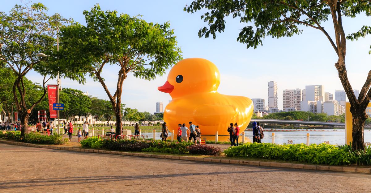 Giant inflatable rubber duck drawing crowds in a vibrant city park setting.