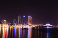 岘港的夜间城市景观充满活力，天际线灯火通明，桥梁倒映在河面上