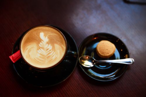 Free A beautifully crafted cappuccino with latte art, accompanied by a small cookie on a dark wooden table. Stock Photo