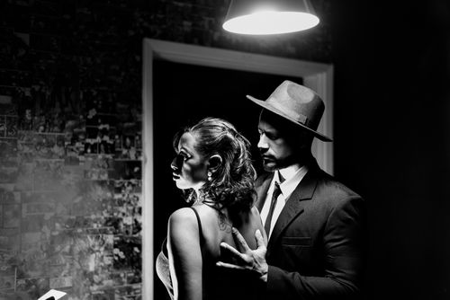 Free A vintage-inspired black and white photo featuring an elegant couple in classic attire beneath a glowing light fixture. Stock Photo