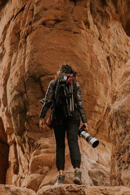 Back view of a female photographer hiking with gear in a rocky cave formation.