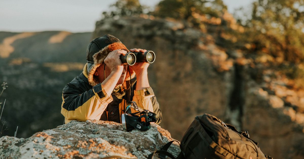 An adventurer looks through binoculars across a canyon at dusk.