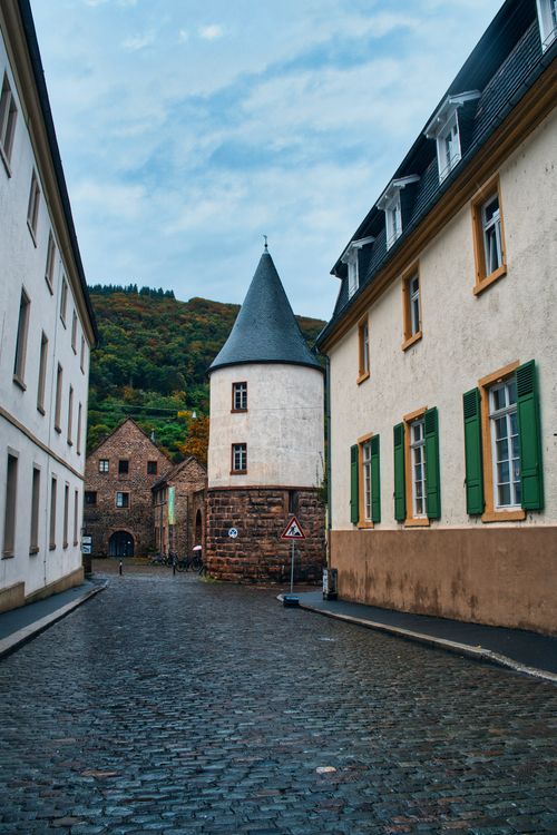 Free Cobblestone street in Heidelberg with historic buildings and tower, charming old town vibe. Stock Photo