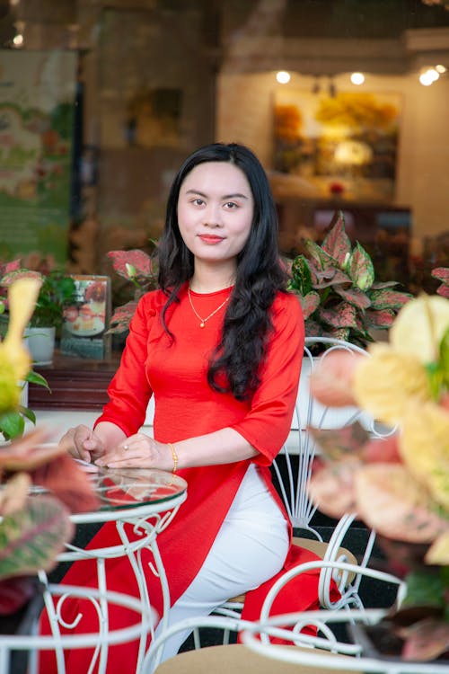 Free A woman in red sitting at a table with flowers Stock Photo