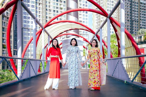 Three women in colorful dresses stand on a bridge