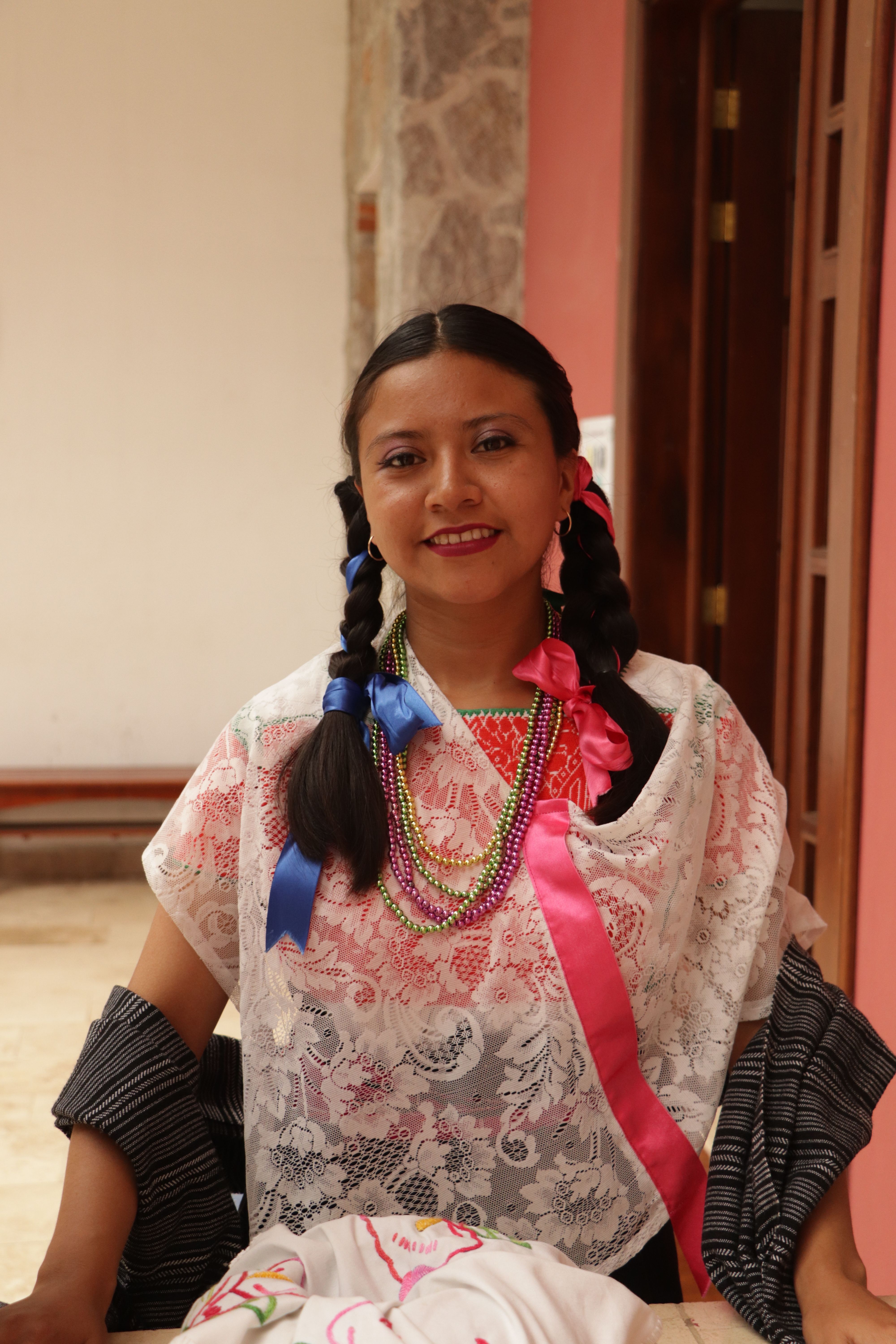 Portrait of a smiling woman in traditional attire with vibrant braided hair and necklaces in Mexico.