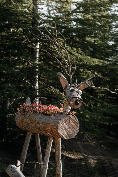 Free Charming handmade wooden reindeer sculpture with floral decoration in a forest landscape. Stock Photo