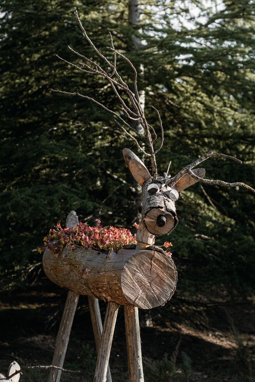 Free Artistic wooden deer sculpture with flowers on a log in a forest. Stock Photo