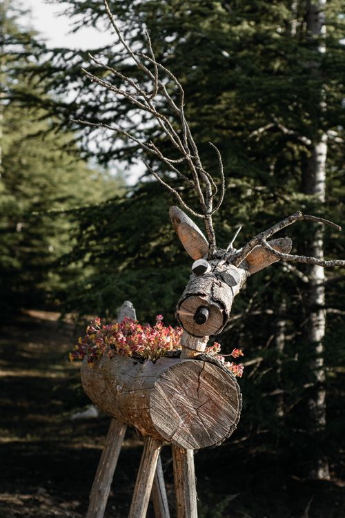 Free A handcrafted wooden reindeer sculpture with flowers, set in a tranquil forest landscape. Stock Photo