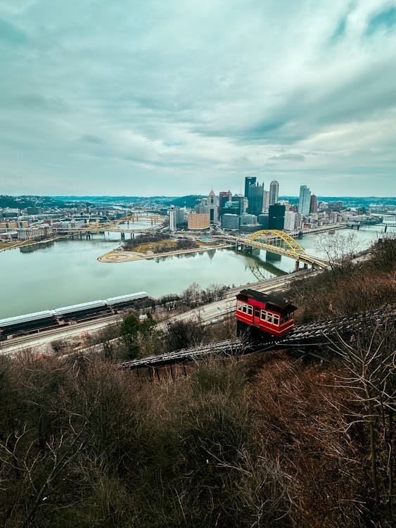 A red train going over a hill with a city in the background