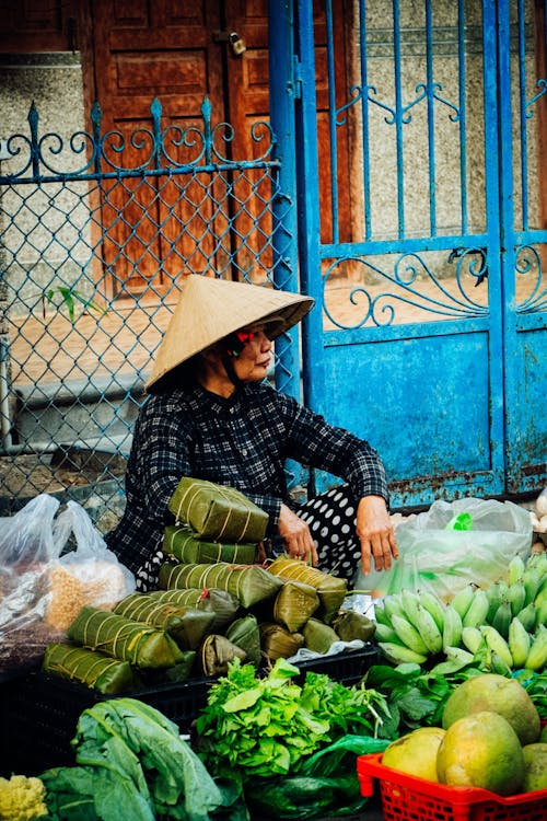 A woman in a conical hat sitting on a bench next to a market