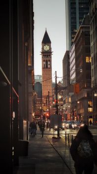 A bustling Toronto street scene with the iconic clock tower illuminated at dusk.