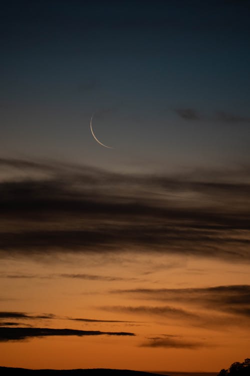 A crescent moon is seen in the sky at sunset