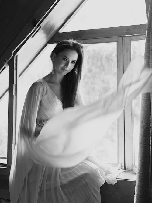 A woman in a wedding dress sitting by a window