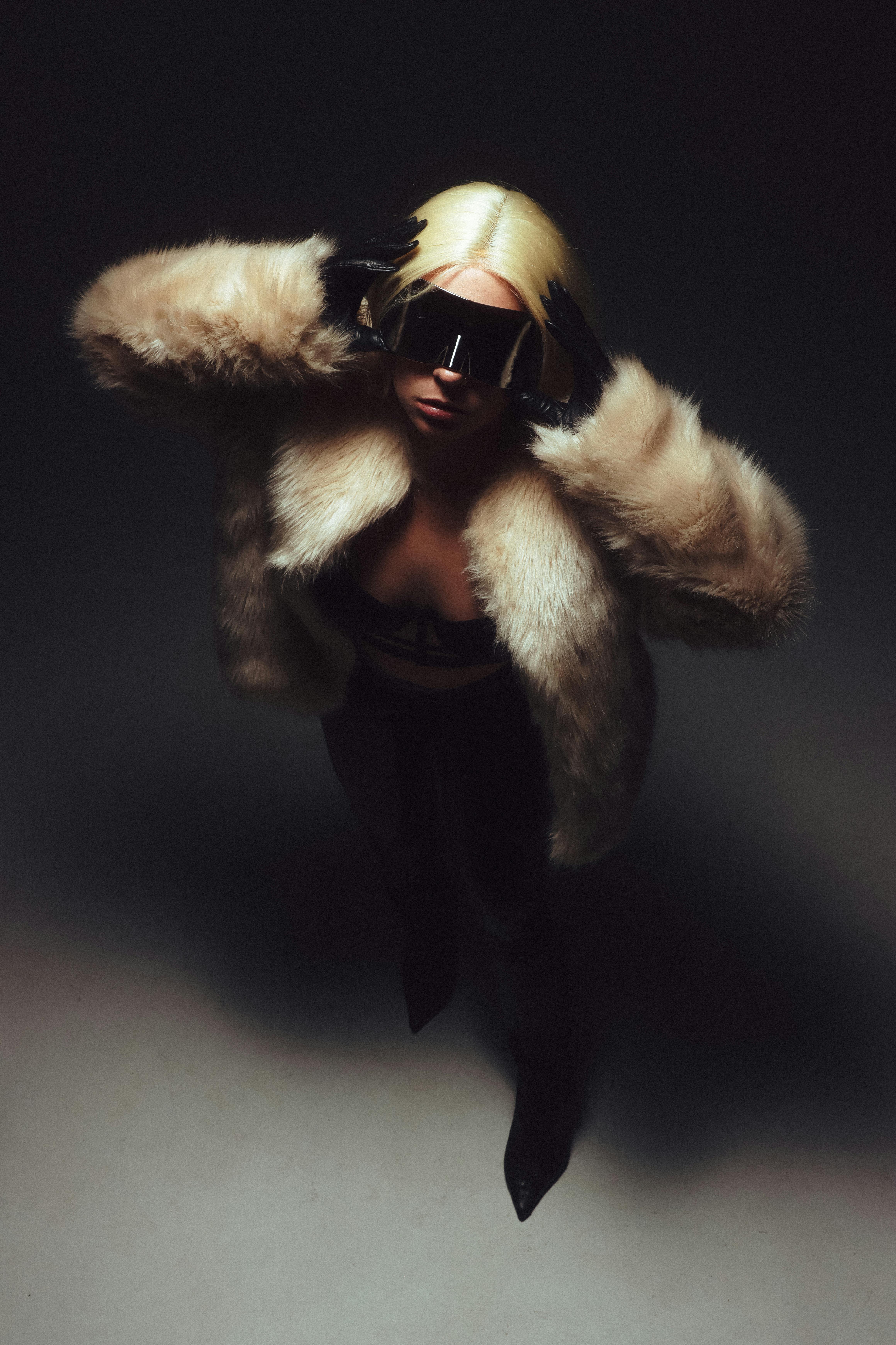 Fashionable woman in a glamorous fur coat and sunglasses posing in a studio setting.