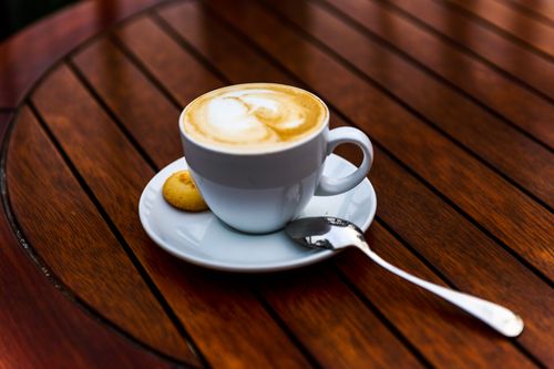 Free A beautifully crafted cappuccino with latte art served with a biscuit on a wooden table. Stock Photo