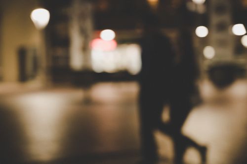 Free Out-of-focus image of a couple walking at night with city lights in the background. Stock Photo