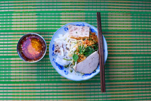 Colorful Vietnamese noodle salad with herbs and dipping sauce on a bamboo mat.