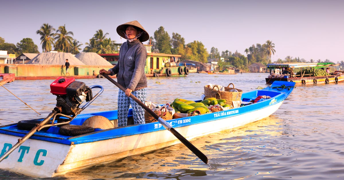 Woman steering a motorized boat filled with goods in vibrant riverine setting.