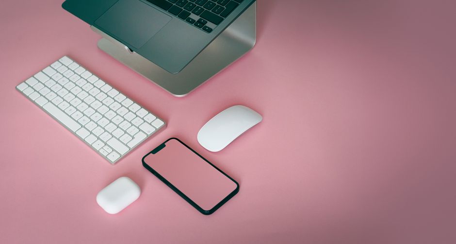 Best Dog Training Apps and Online Courses Compared: Features and Value A minimalist desk setup featuring a laptop, keyboard, mouse, and smartphone on a pink background.