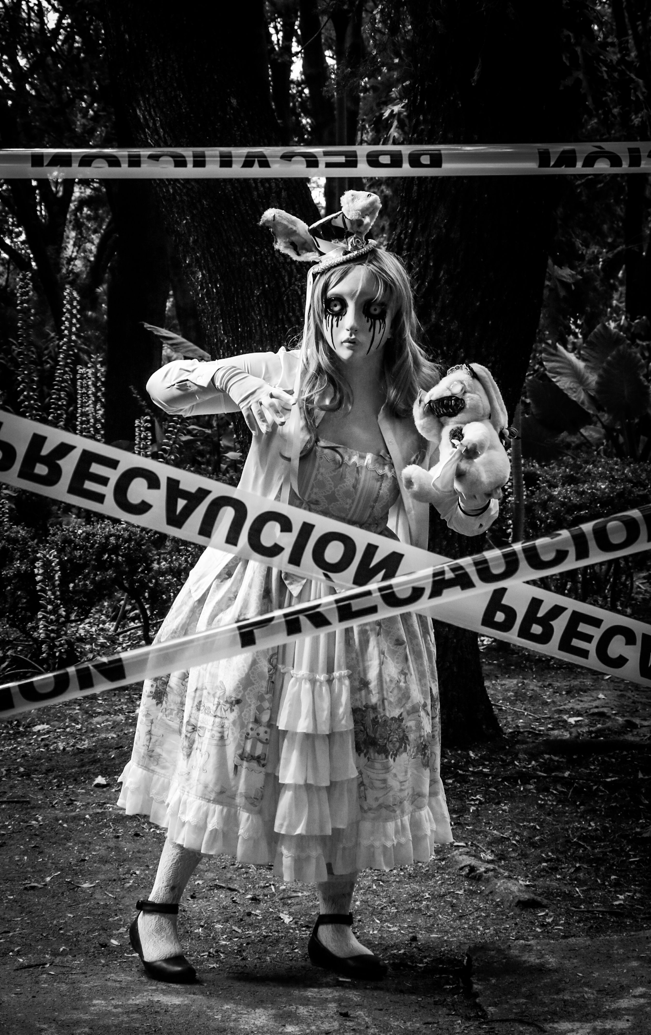 Creepy woman in doll costume holding teddy bear in eerie forest.