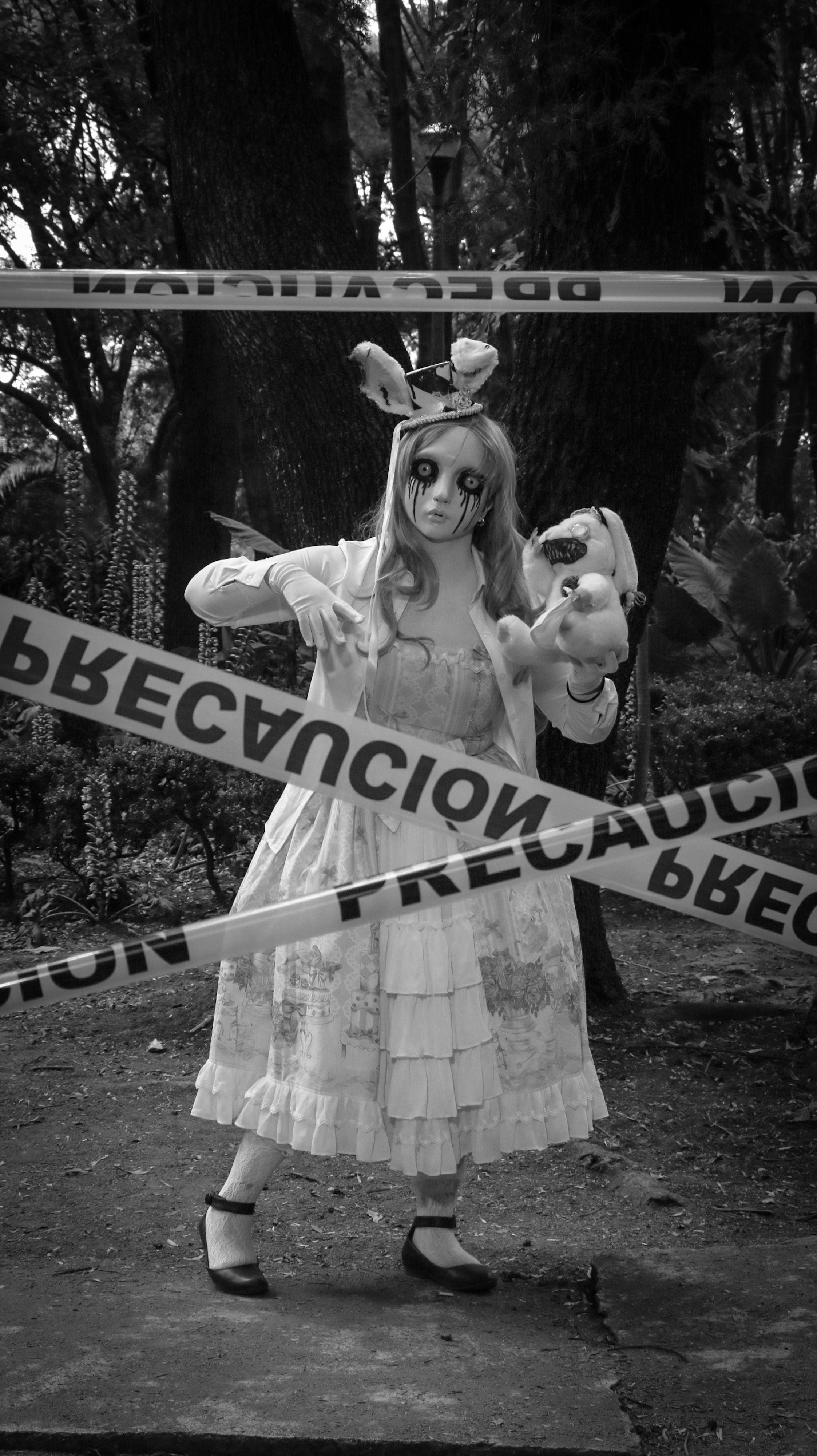 Chilling black and white photo of a person in a spooky doll costume behind caution tape.