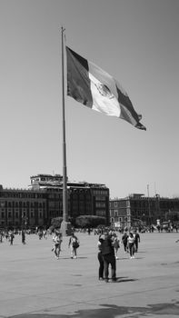 A vibrant scene at the Zócalo in Mexico City featuring the Mexican flag and a bustling crowd.