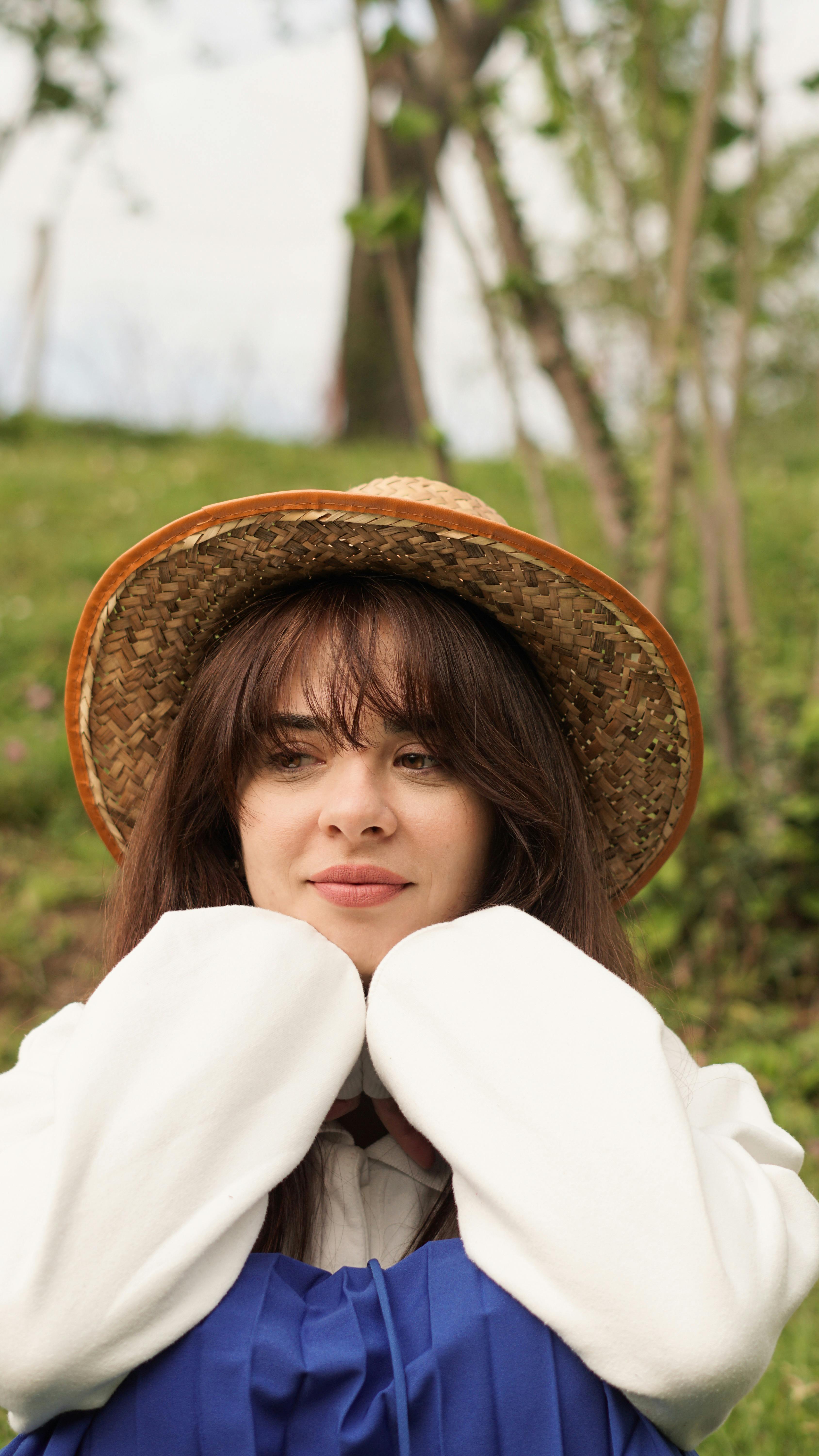 A young woman in a straw hat enjoys a sunny day outdoors, showcasing fashion and relaxation.